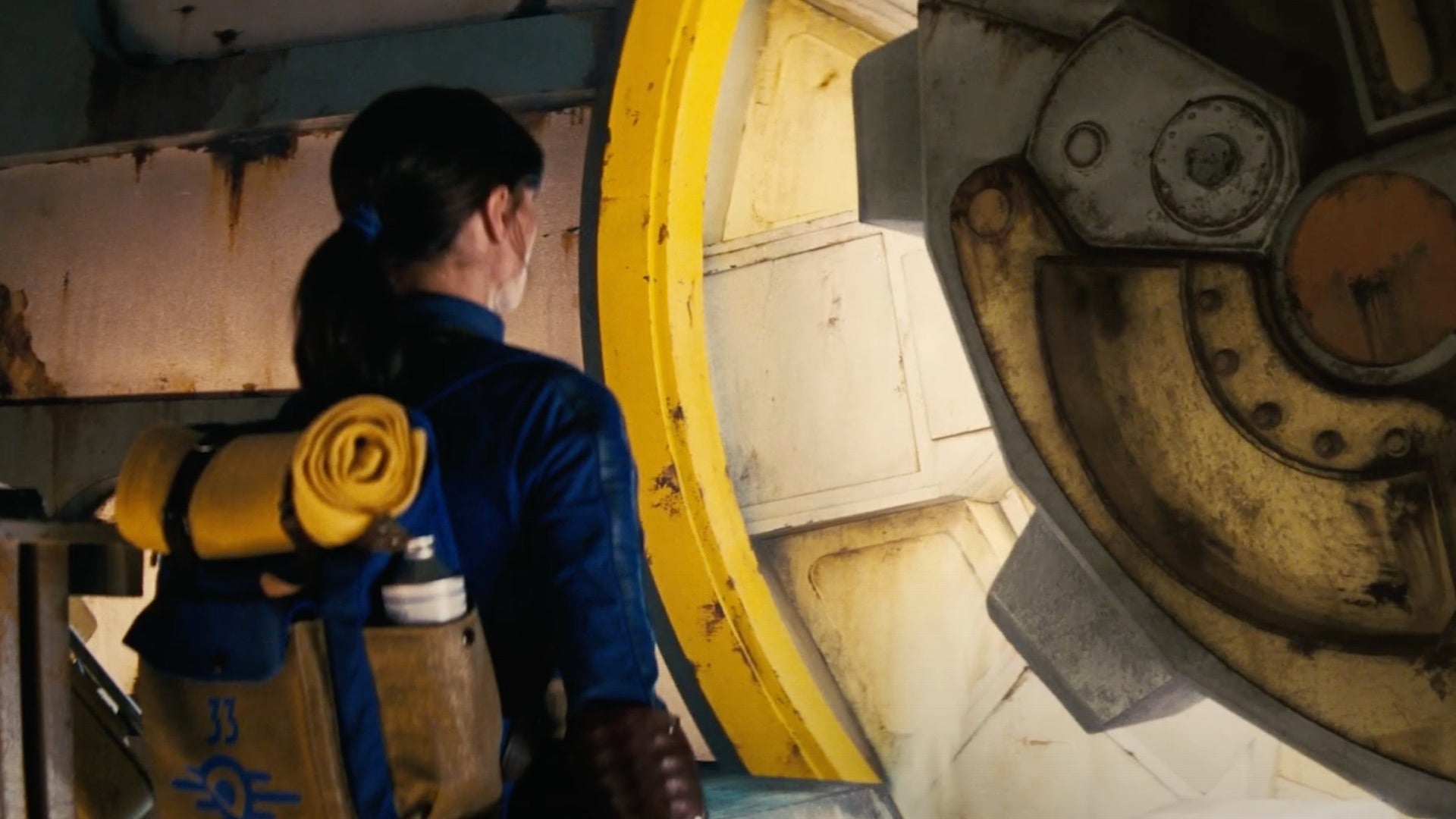Un'immagine dal trailer della serie TV di Fallout che mostra un Vault Dweller, interpretato da Ella Purnell, che aspetta mentre si apre una porta del Vault.