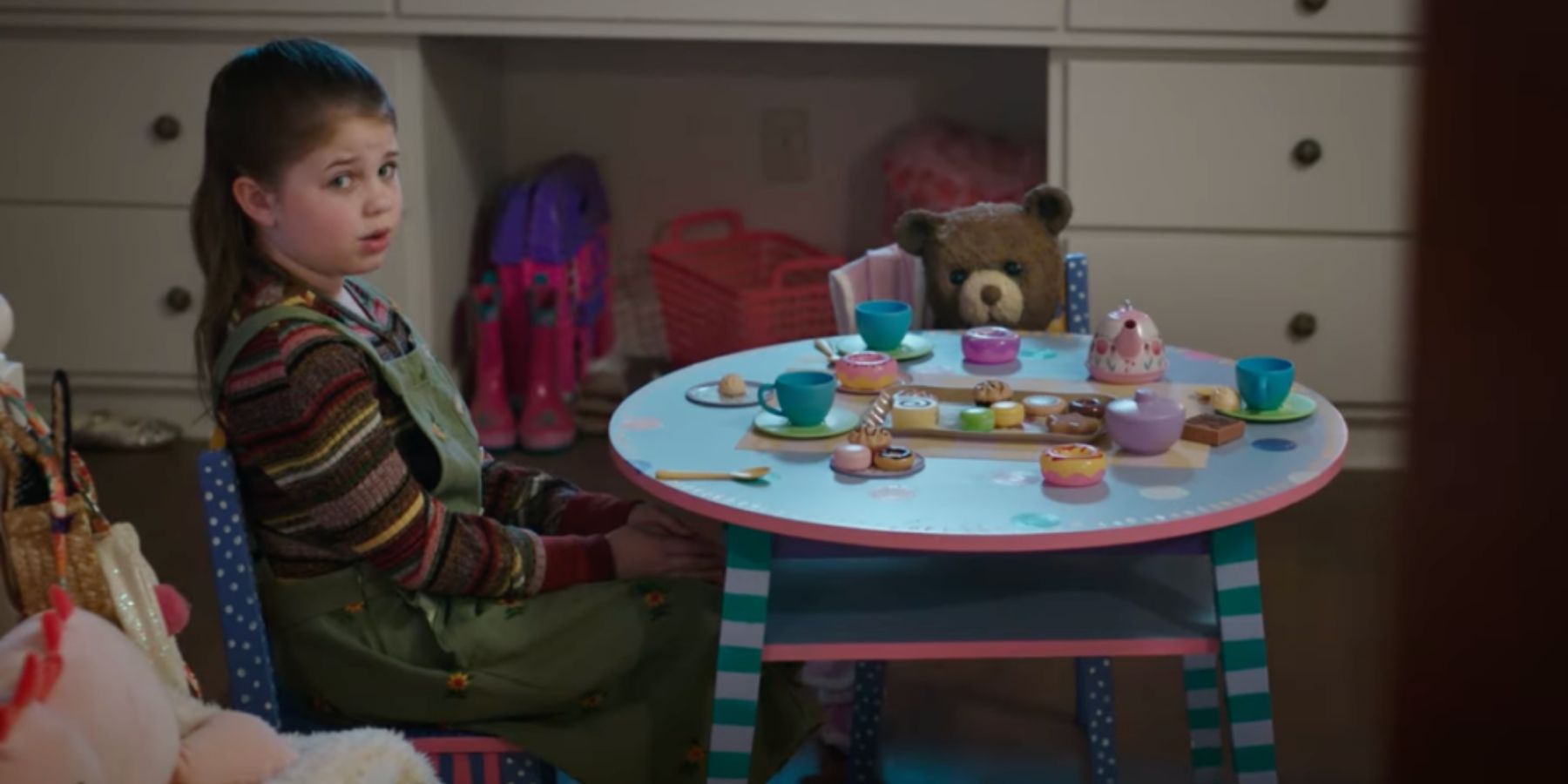 Alice (Piper Braun) sitting at a table with the bear in Imaginary