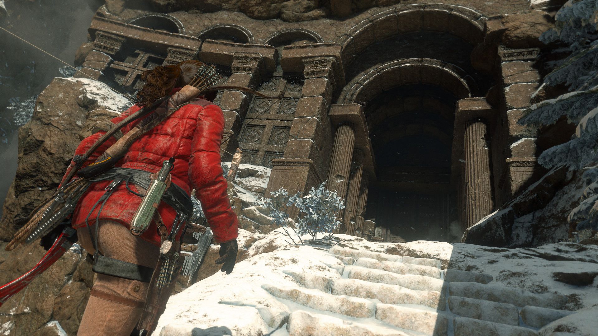 Lara Croft dans une veste d'hiver rouge montant les marches enneigées d'un temple dans Rise of the Tomb Raider.