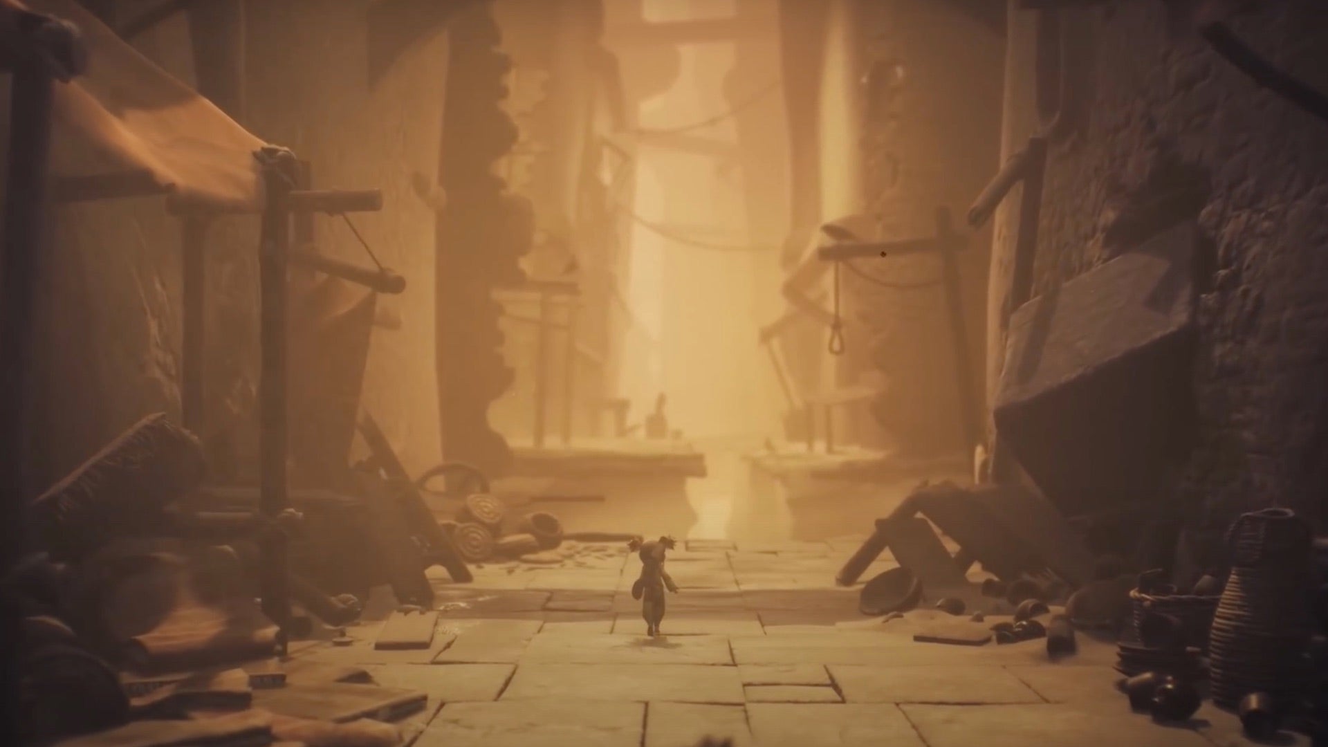 Capture d'écran de Little Nightmares 3 montrant l'un de ses deux protagonistes marchant le long des rues sablonneuses d'une ancienne cité en ruine, des étals de marché effondrés de chaque côté.