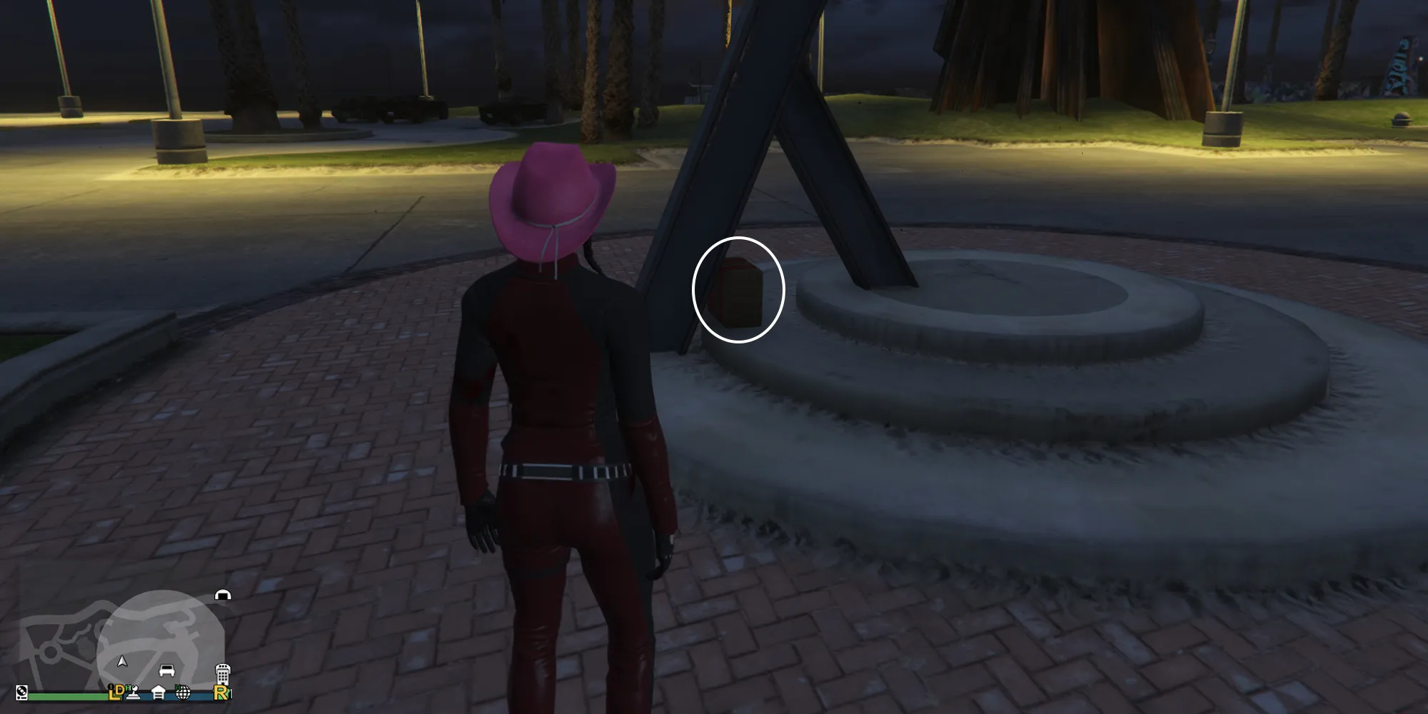 GTAオンラインの女性プレイヤーがベスプッチビーチスケートパークにいます。底部で'Y'の形に分かれる金属の彫刻を正面にしています。３段のサークルがある円形のコンクリートのプラットフォームの間の隙間にG'sキャッシュがあります。