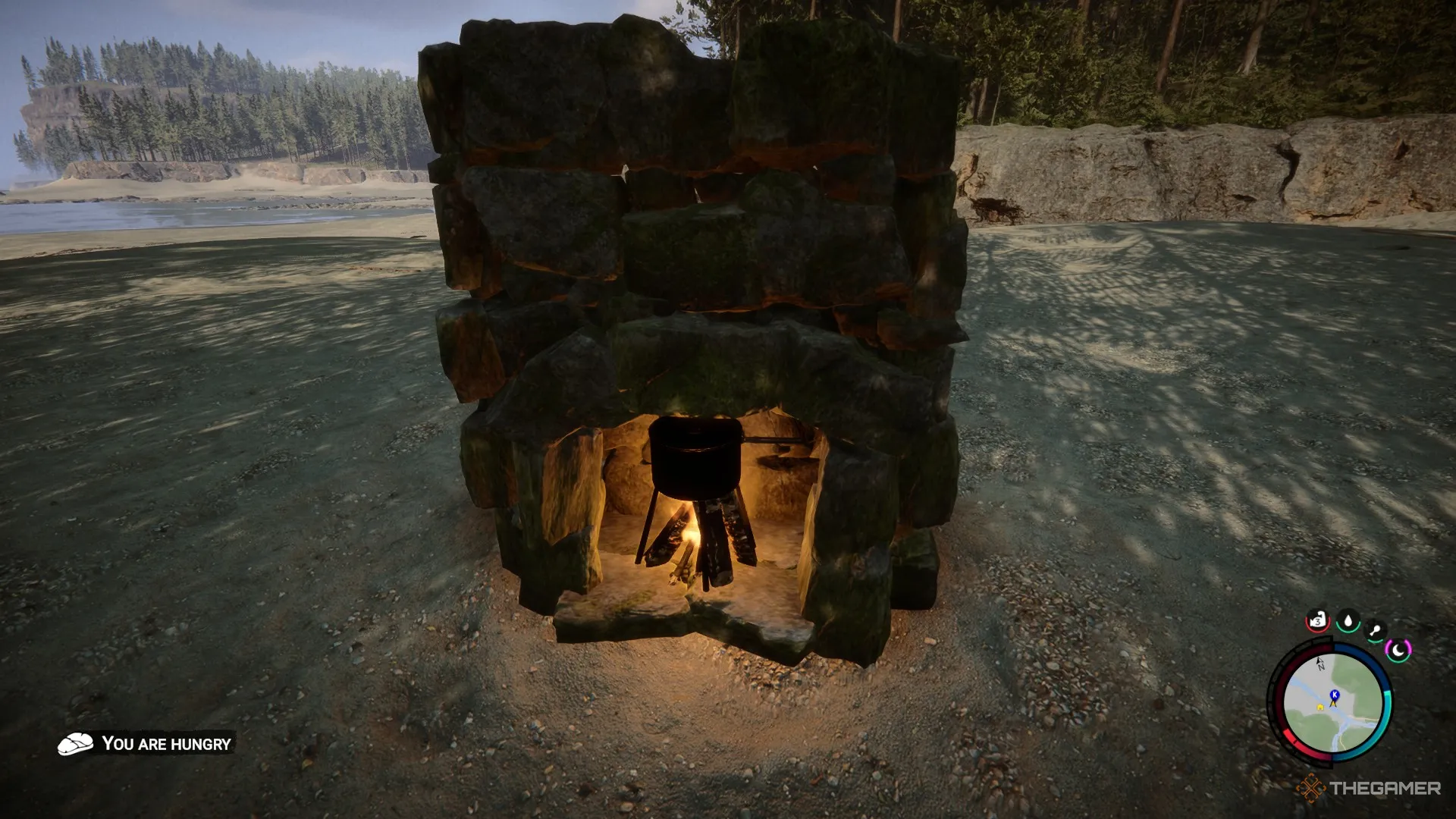 A screenshot from Sons of the Forest showing a fire with a cooking pot on top in a Stone fireplace resting on a beach.