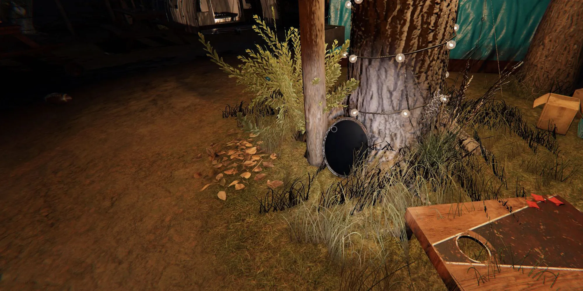 Image depicts a haunted mirror on the ground next to a tree with fairy lights on it on Camp Woodwind in Phasmophobia. 