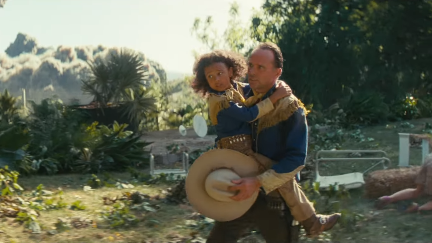 Walton Goggins nei panni di Cooper Howard nella serie TV di Fallout di Amazon tiene in braccio un bambino mentre scappa da un'esplosione