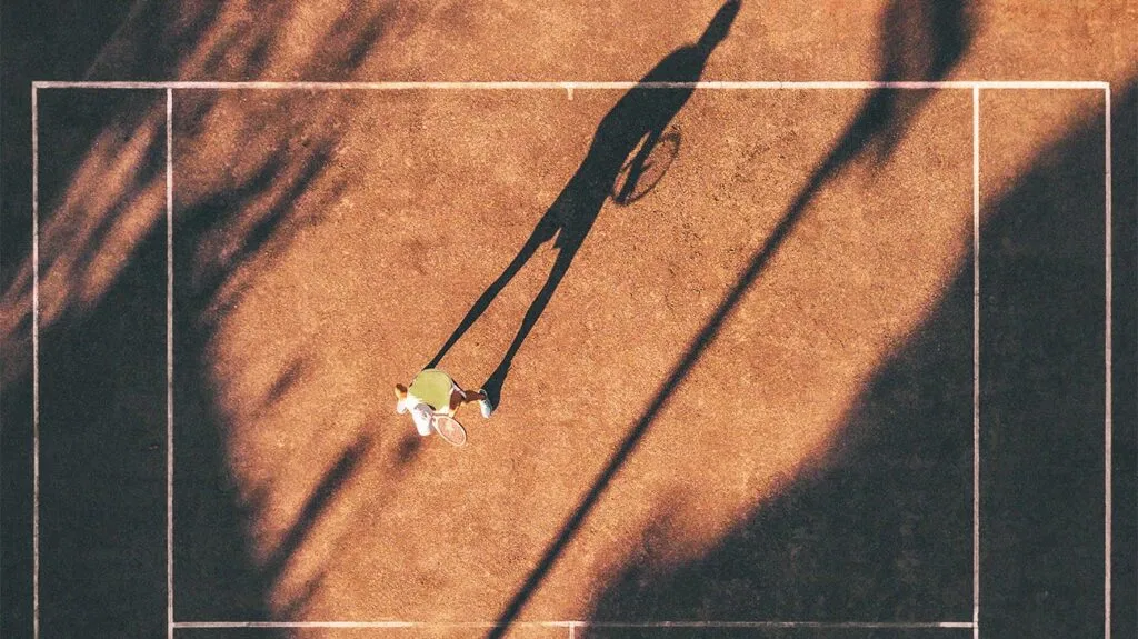 Visão aérea de uma pessoa em uma quadra de tênis ao ar livre sob o sol