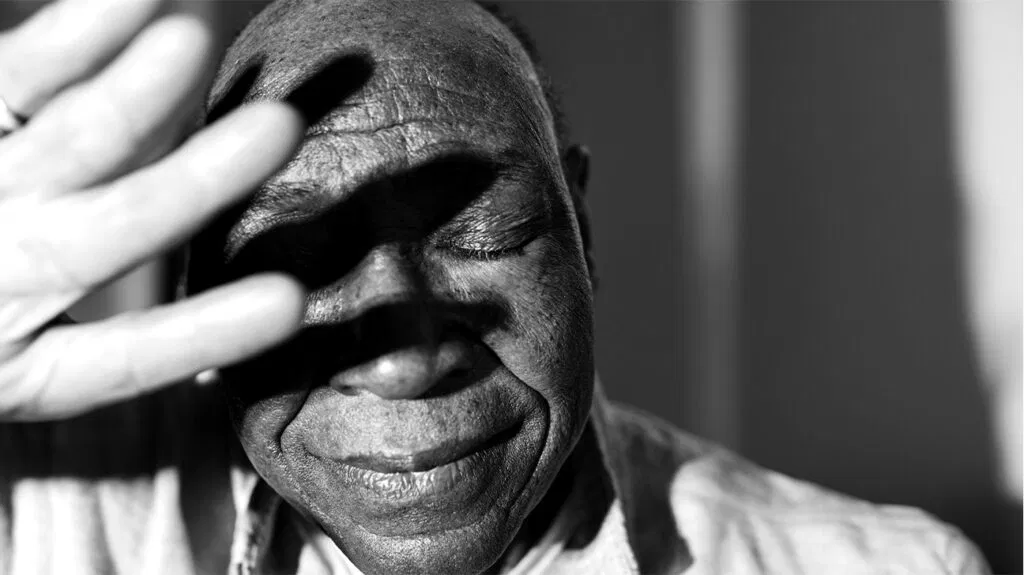 Photo en noir et blanc d'un homme noir plus âgé se protégeant le visage avec sa main