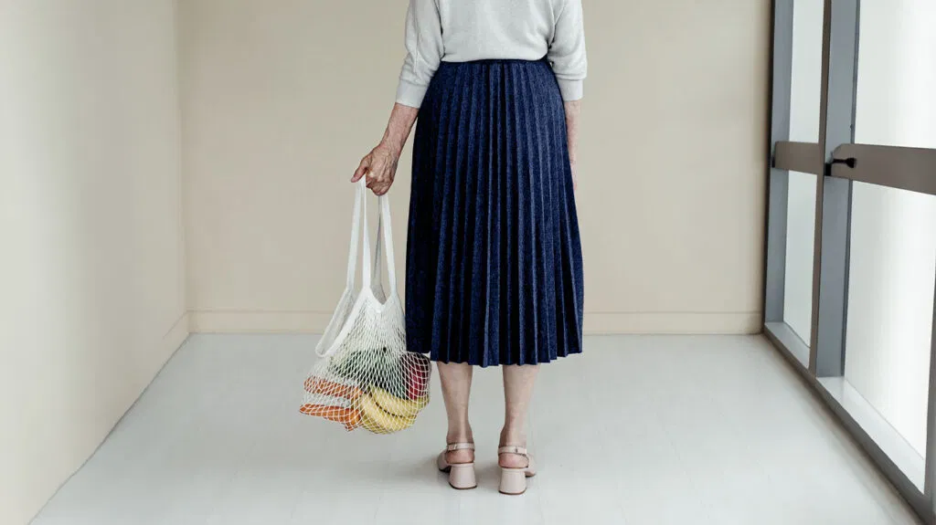 Una donna che tiene in mano una borsa della spesa piena di verdure e frutta.