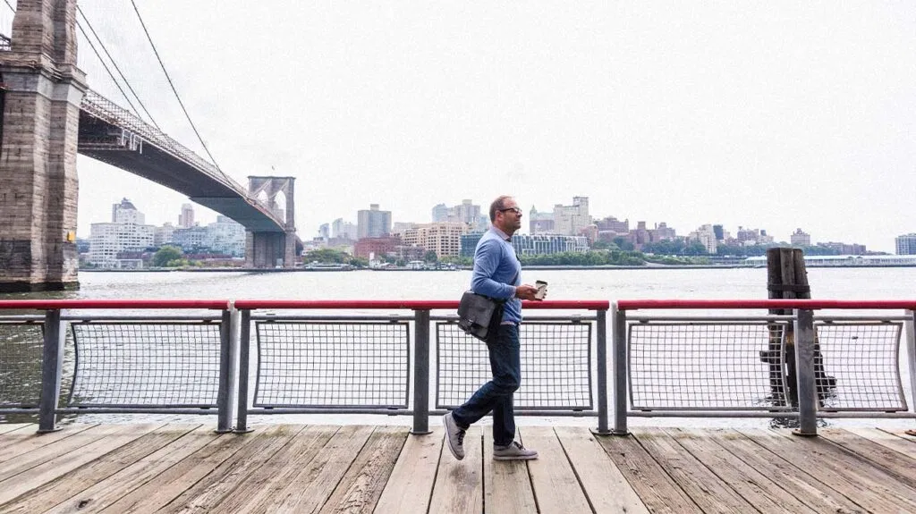 Uomo che cammina vicino al Brooklyn Bridge tenendo in mano un caffè