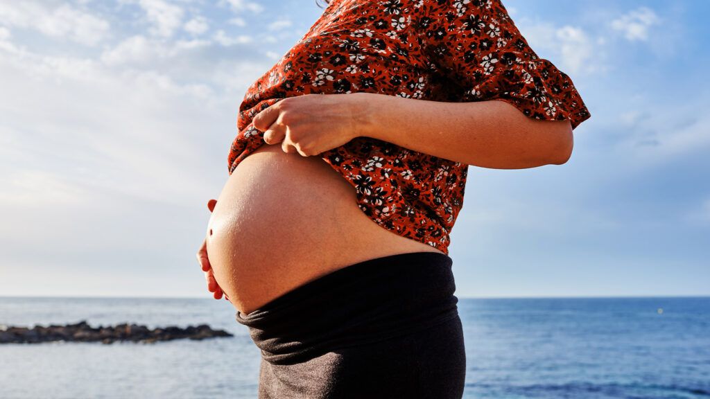Une femme montre son ventre de femme enceinte en se tenant sur une rive