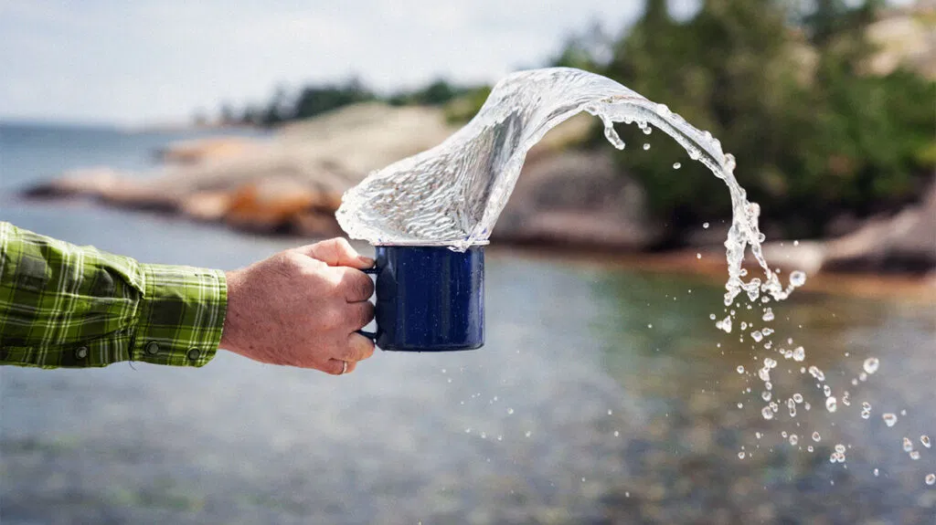 Una persona sciacqua una tazza con acqua in un lago