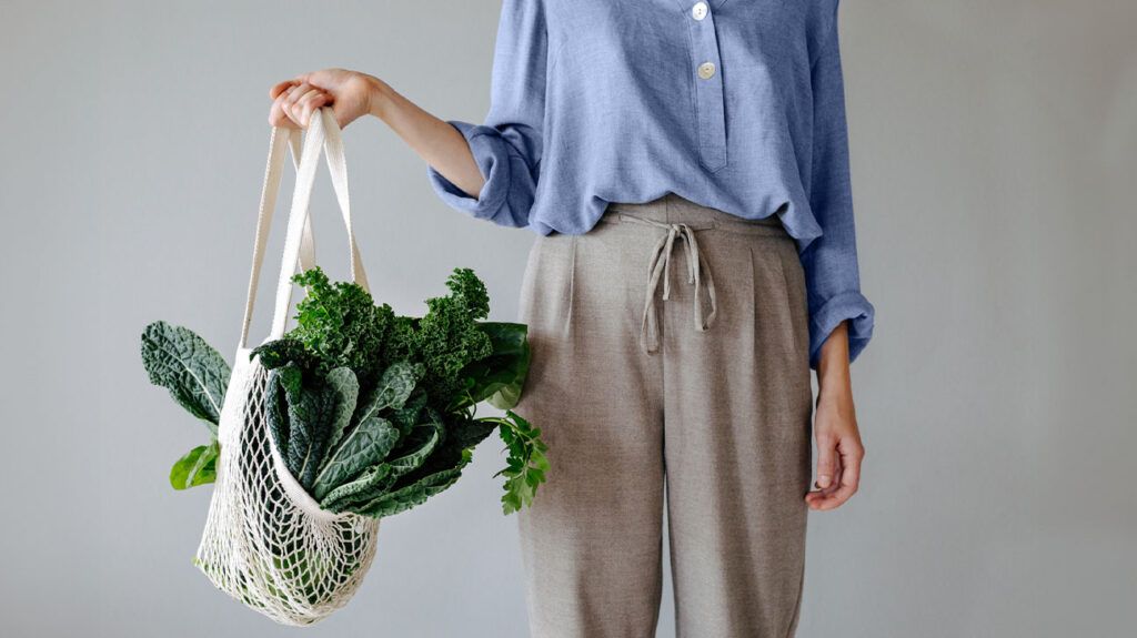 Uno primo piano di una donna che tiene una borsa per la spesa con verdure a foglia verde scuro
