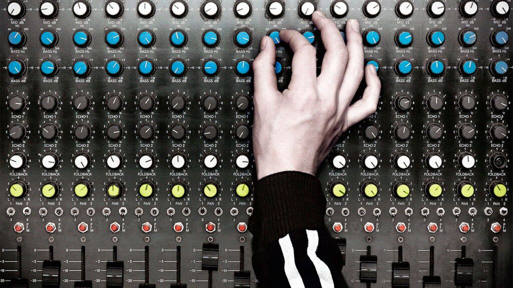 Une main tourne un bouton sur une table de mixage audio
