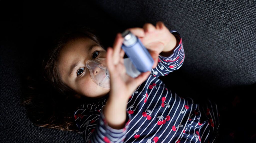 Un bambino che usa un inalatore per l'asma giace per terra