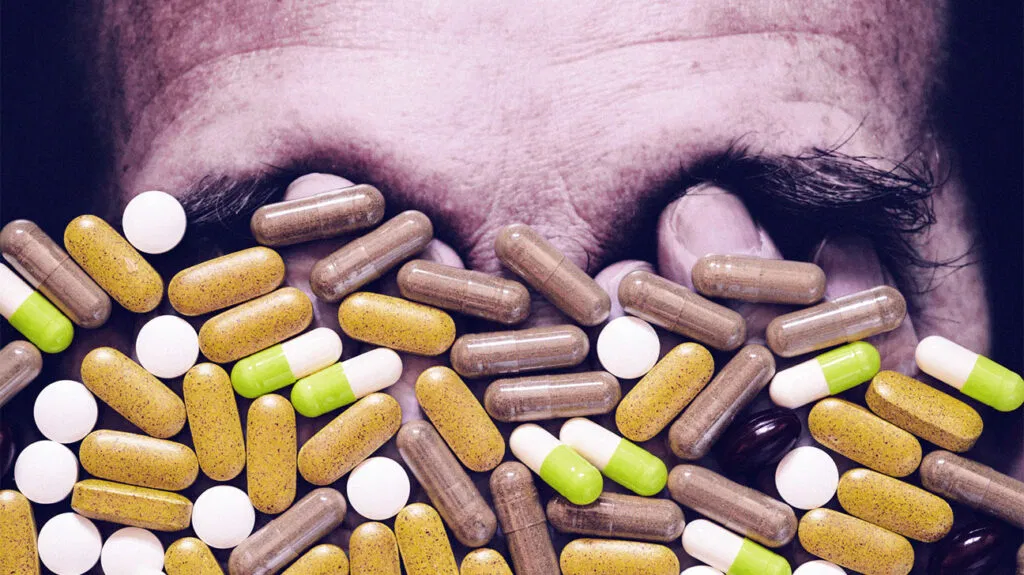 Various pills and medications are scattered in front of a man’s face