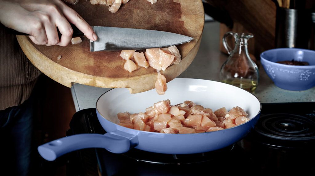 A person cooking diced chicken breast in a pan, which is a good source of vitamin B