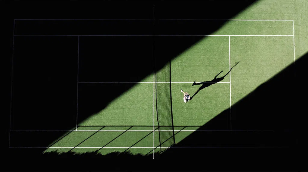 Una ripresa aerea di una partita di tennis dall'alto con l'ombra del giocatore riflessa sul campo