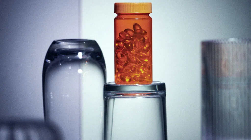 Una bottiglia di vitamine si trova sulla cima di un bicchiere d'acqua