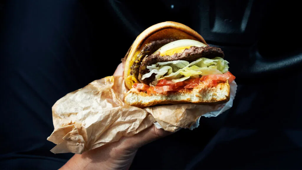 Una persona tiene un cheeseburger doble con cebolla, lechuga y tomate