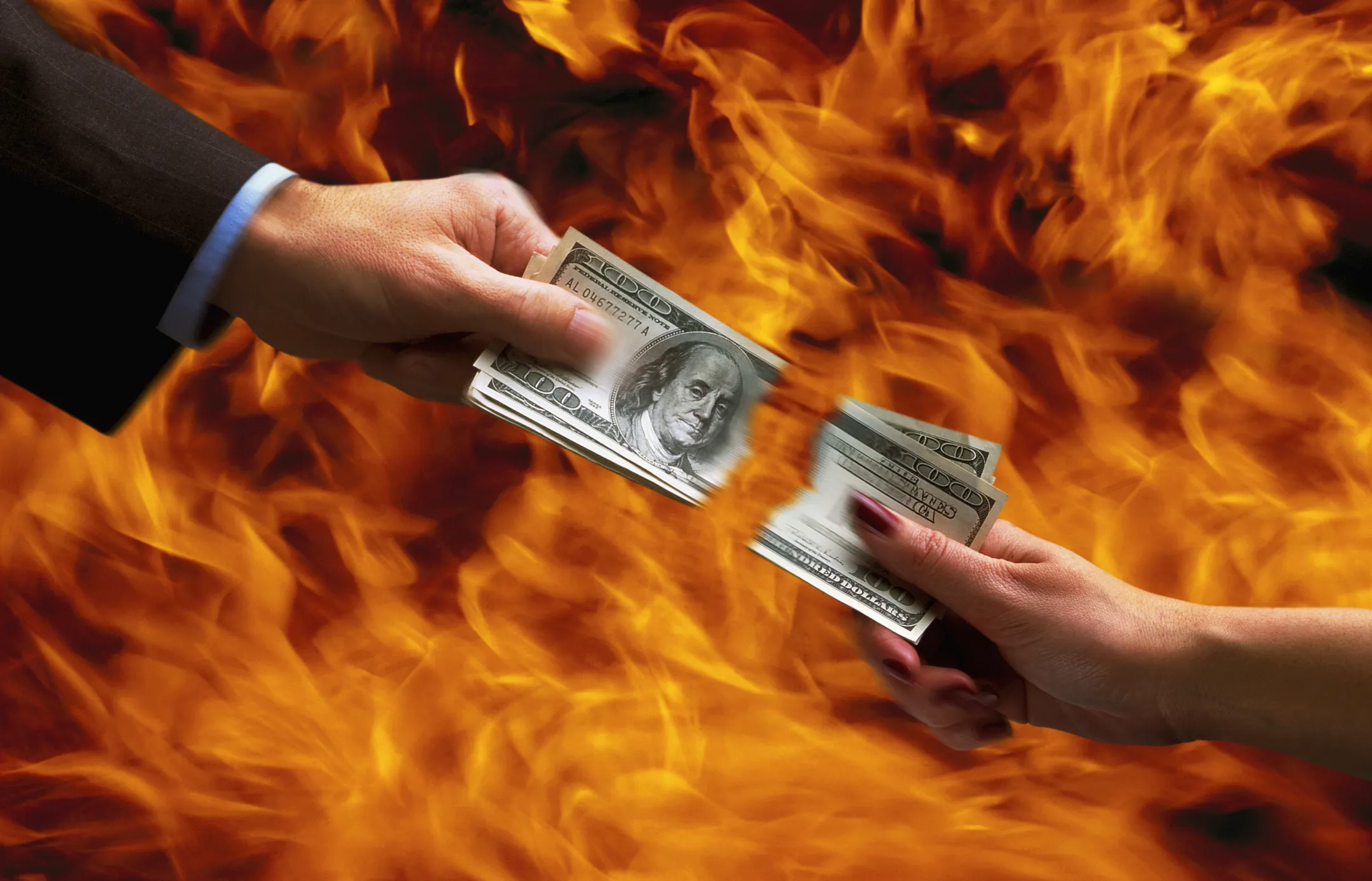 mani di due persone che strappano denaro con fiamme sullo sfondo