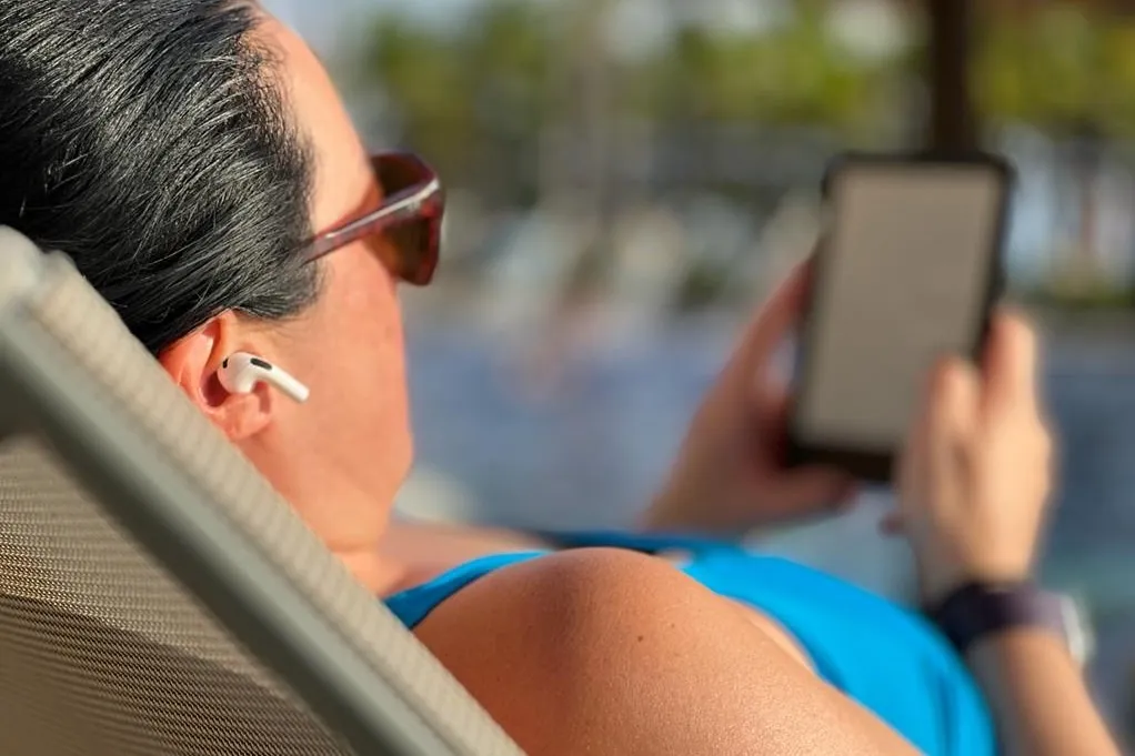 Donna in piscina con auricolari Apple AirPods e un e-reader.