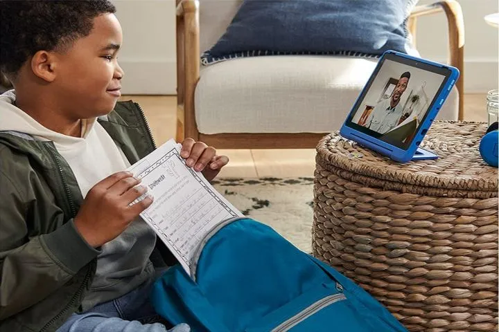 Un bambino con un foglio di lavoro che guarda un video su un tablet Amazon Fire HD 10 Kids Pro blu.