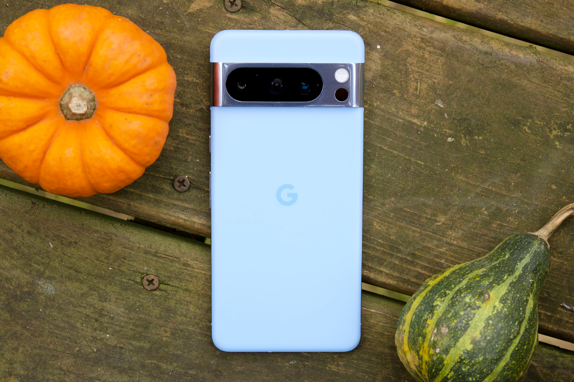 Um Google Pixel 8 Pro azul, deitado de bruços ao lado de uma pequena abóbora e uma abóbora.