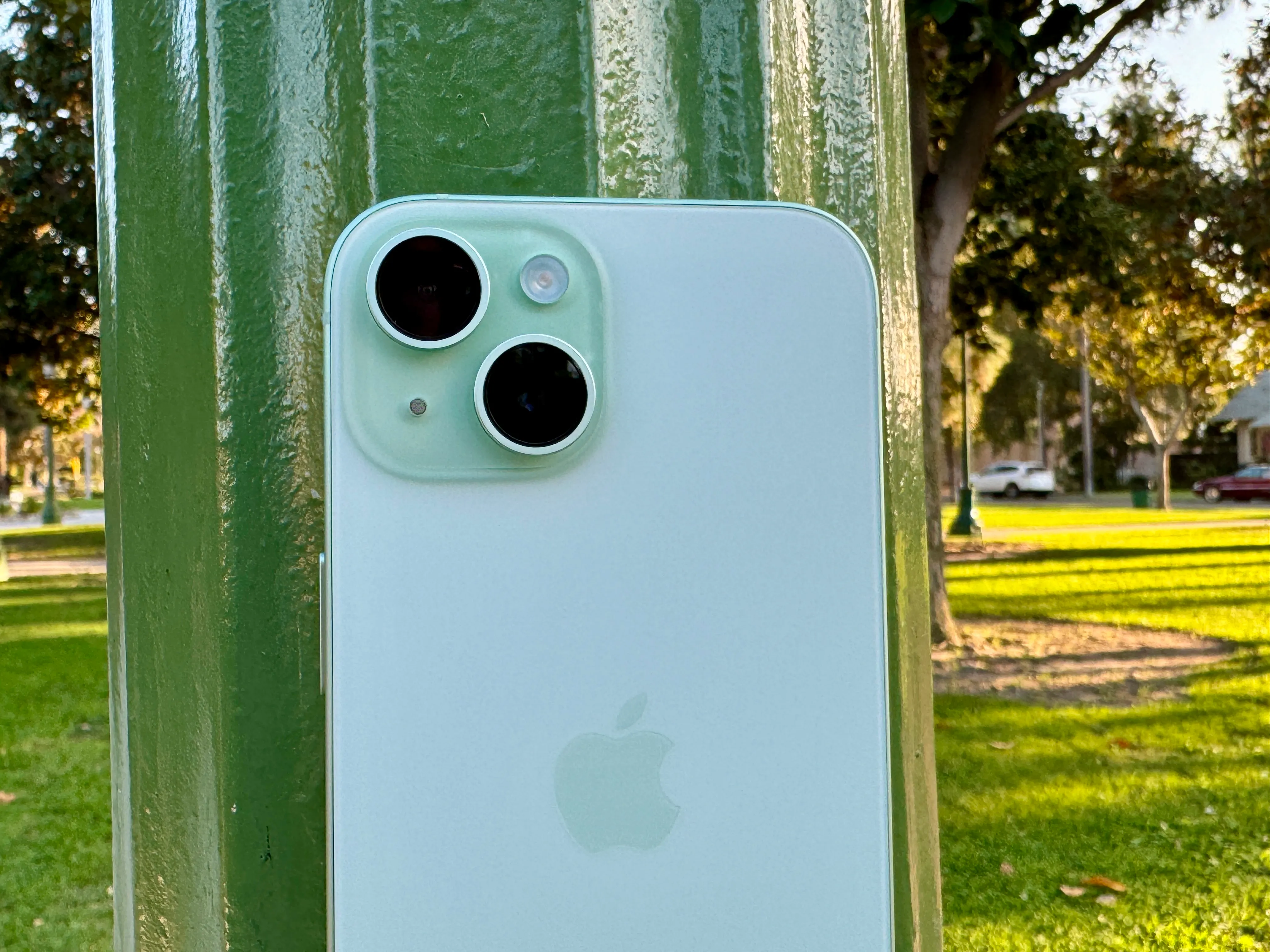 Um iPhone 15 verde apoiado em um poste de luz.