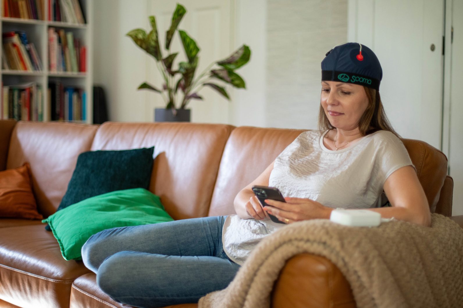 Женщина, сидящая на диване с устройством для стимуляции мозга