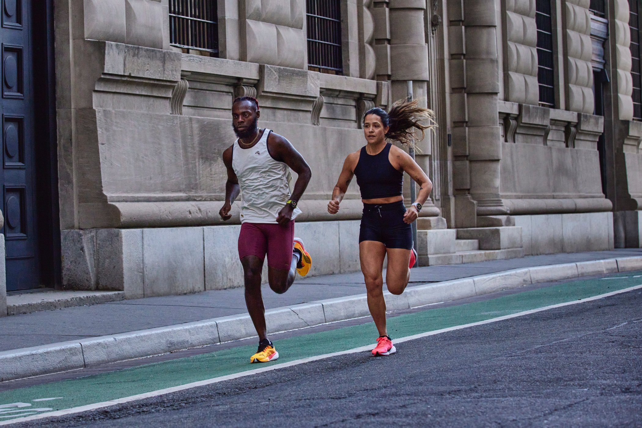 Dos personas corriendo en una calle de la ciudad usando relojes inteligentes Garmin Forerunner 965 y 265.