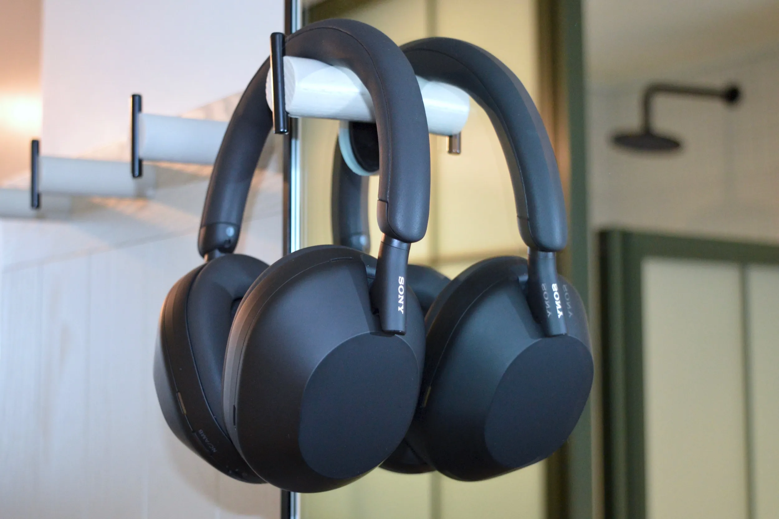 Sony WH-1000XM5 fones de ouvido sem fio pendurados em gancho na parede em frente a um espelho.