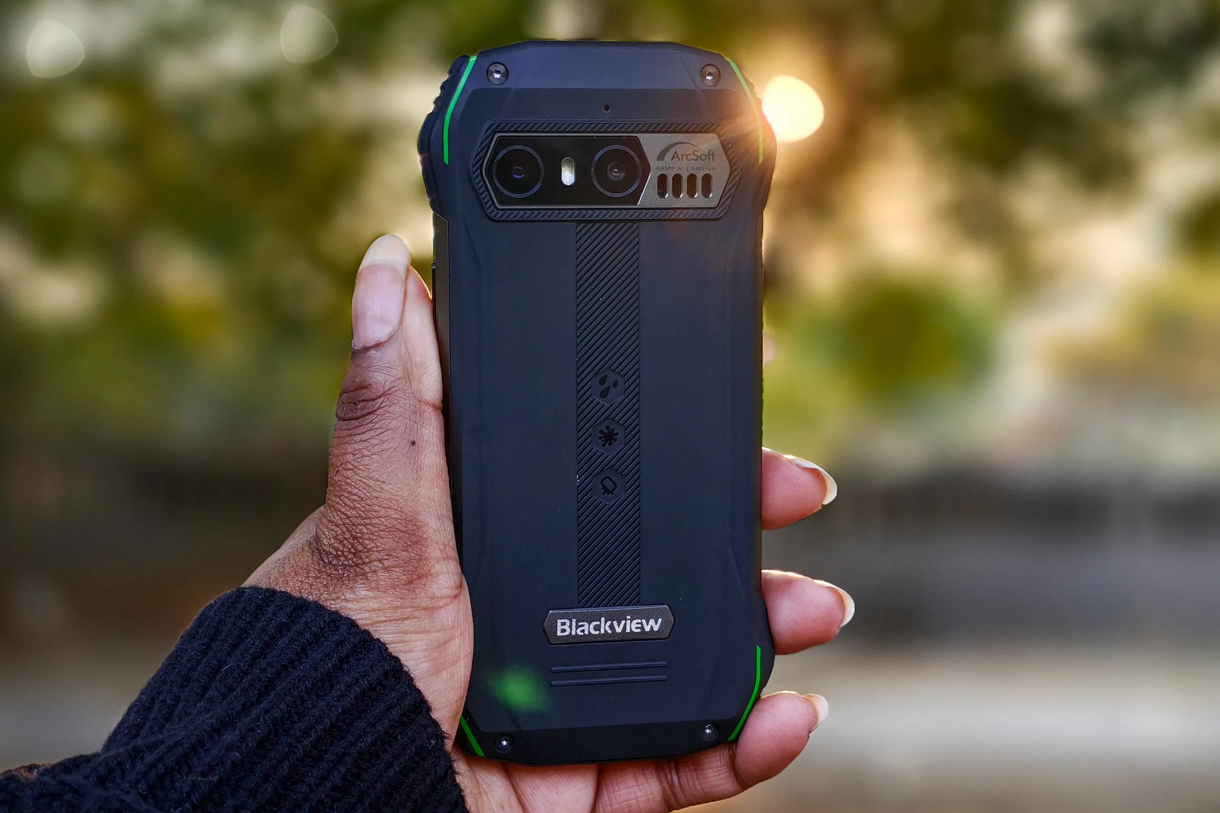 Person holding Blacview N6000 tiny rugged Android phone in hand against the setting sun peaking through trees.