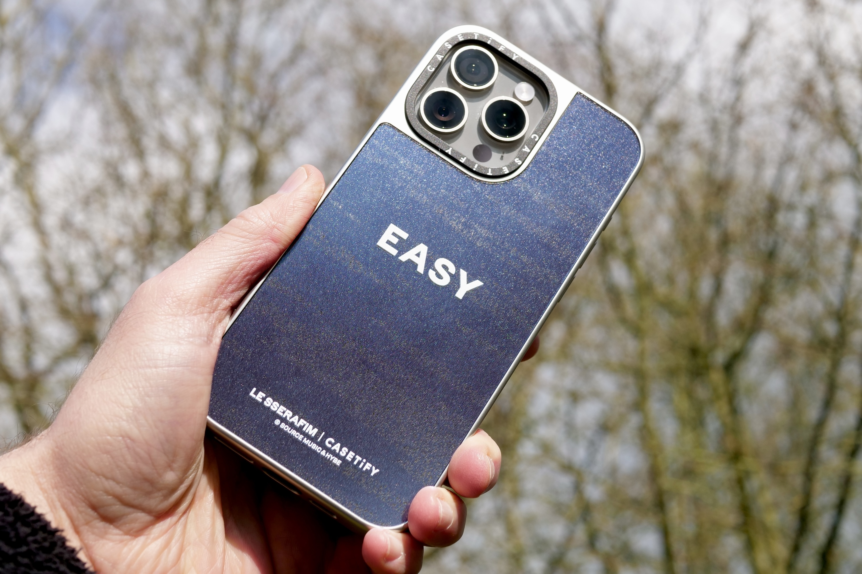 一位拿着带有Casetify x Le Sserafim手机壳的iPhone 15 Pro Max的人。