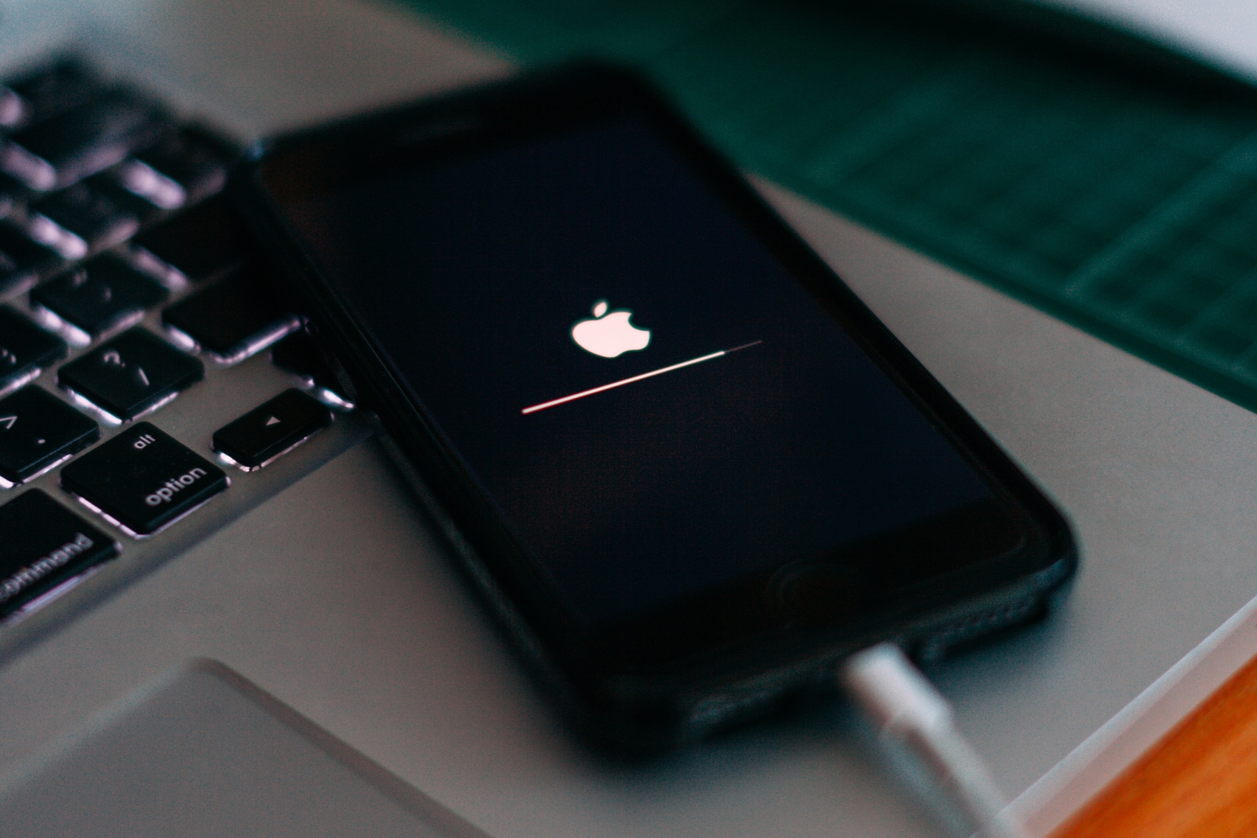 iPhone collegato sopra MacBook che mostra il logo Apple durante un recupero di aggiornamento software.