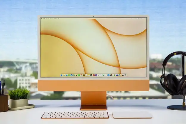Apple iMac de 24 polegadas colocado em uma mesa em um contexto ensolarado.