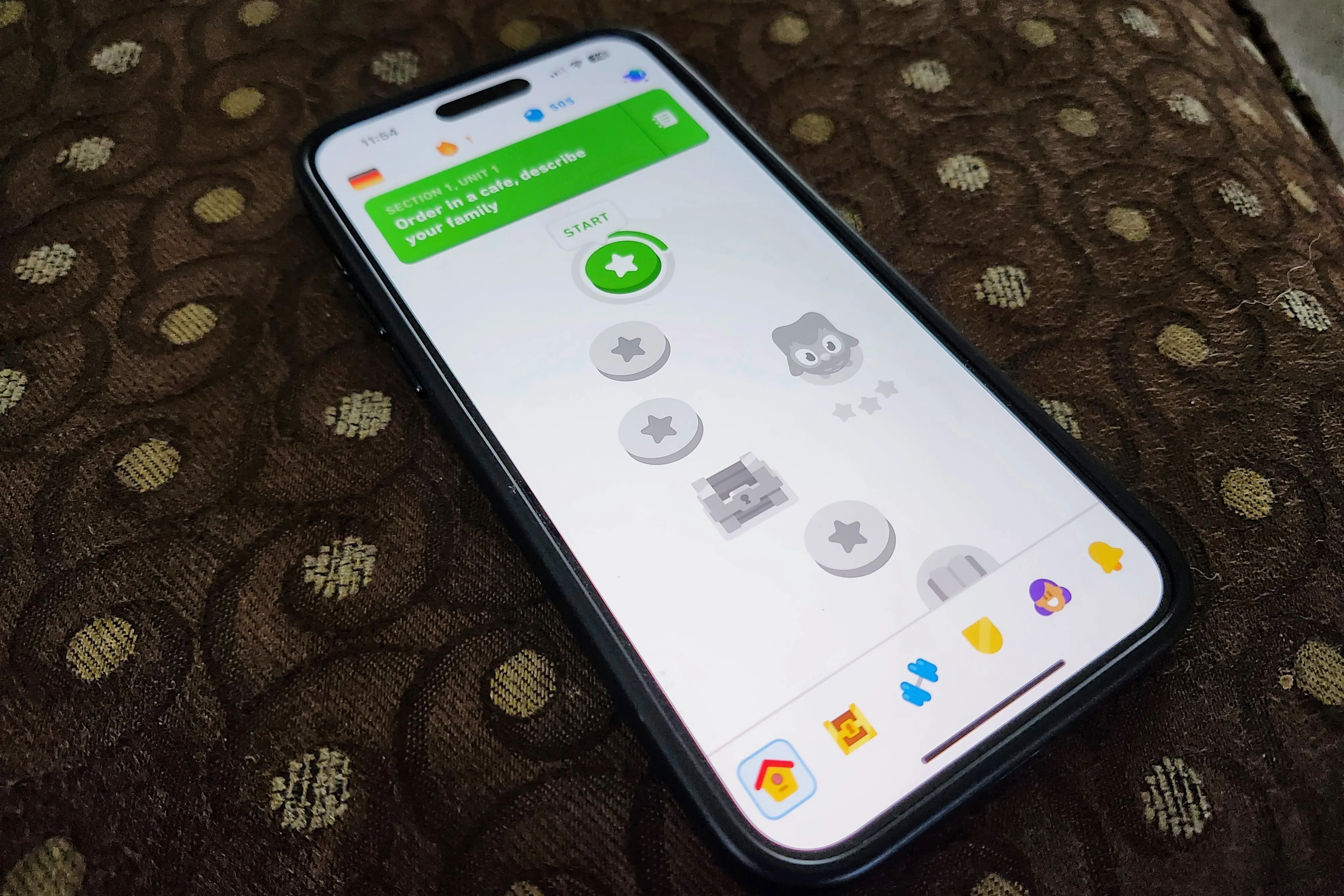 Un iPhone 15 Pro Max mostrando la aplicación Duolingo en un otomano.