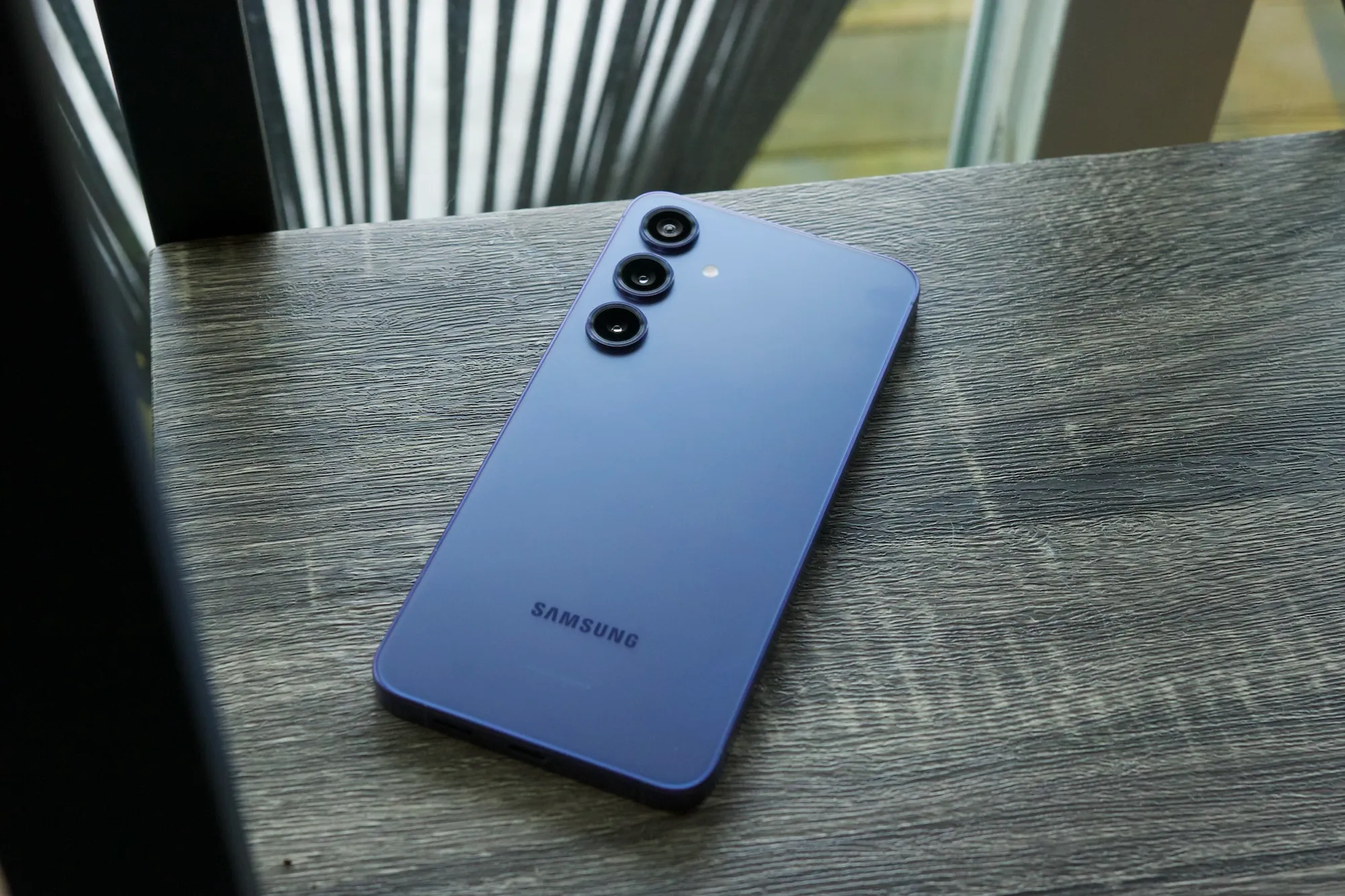Um Samsung Galaxy S24 Plus violeta deitado com a tela para baixo em uma prateleira.