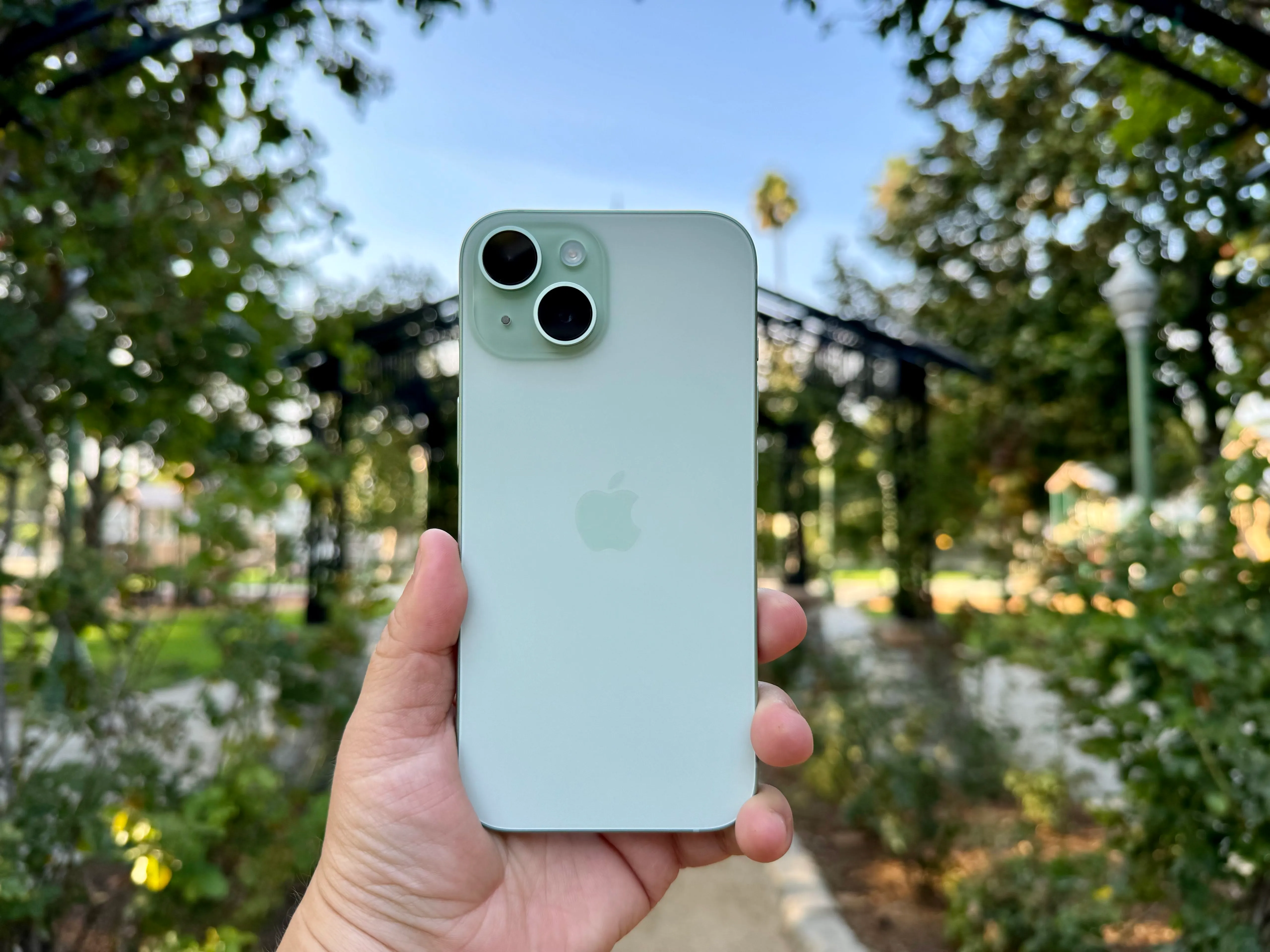 在玫瑰花园中拿着一款绿色的iPhone 15。