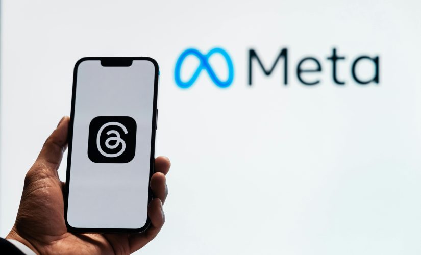Imagen de un ícono de Threads en un teléfono inteligente con un logotipo de Meta en el fondo
