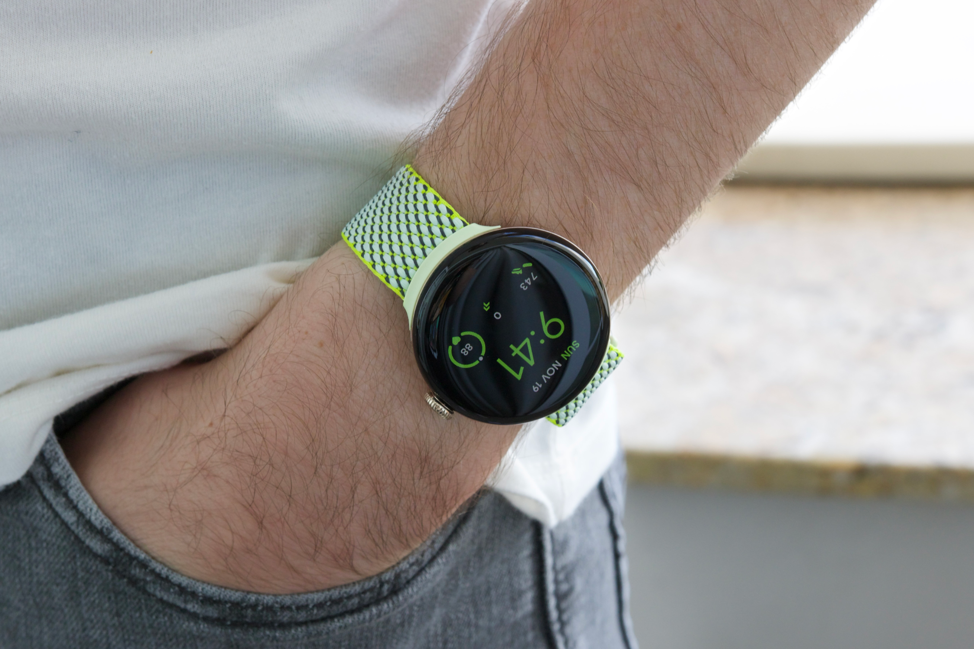 Alguém usando o Google Pixel Watch 2 com uma pulseira de tecido amarelo/verde.