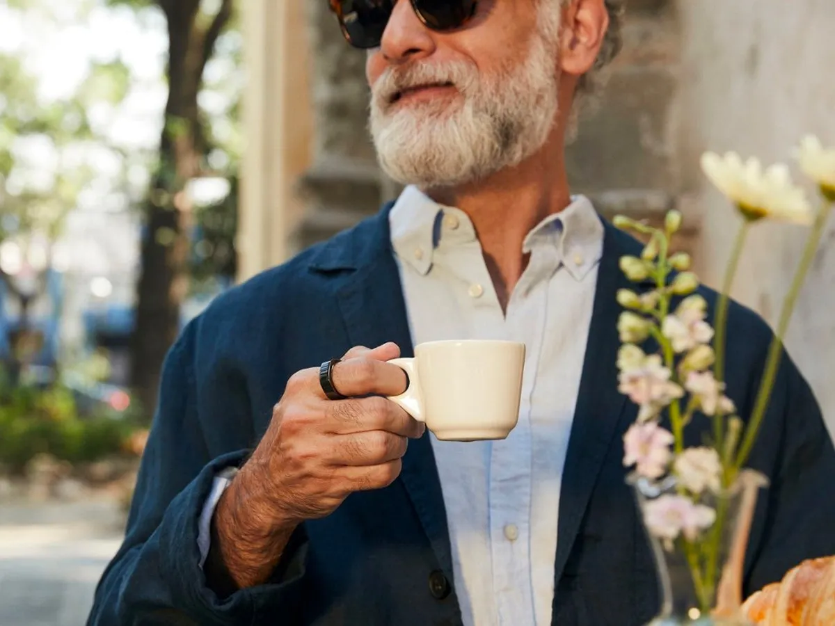 Um homem usa um Oura Ring Gen3 enquanto bebe café em um café.